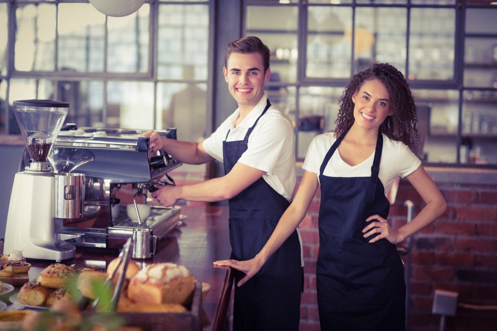 Portrait of smiling waitress in front of colleague making coffee at coffee shop